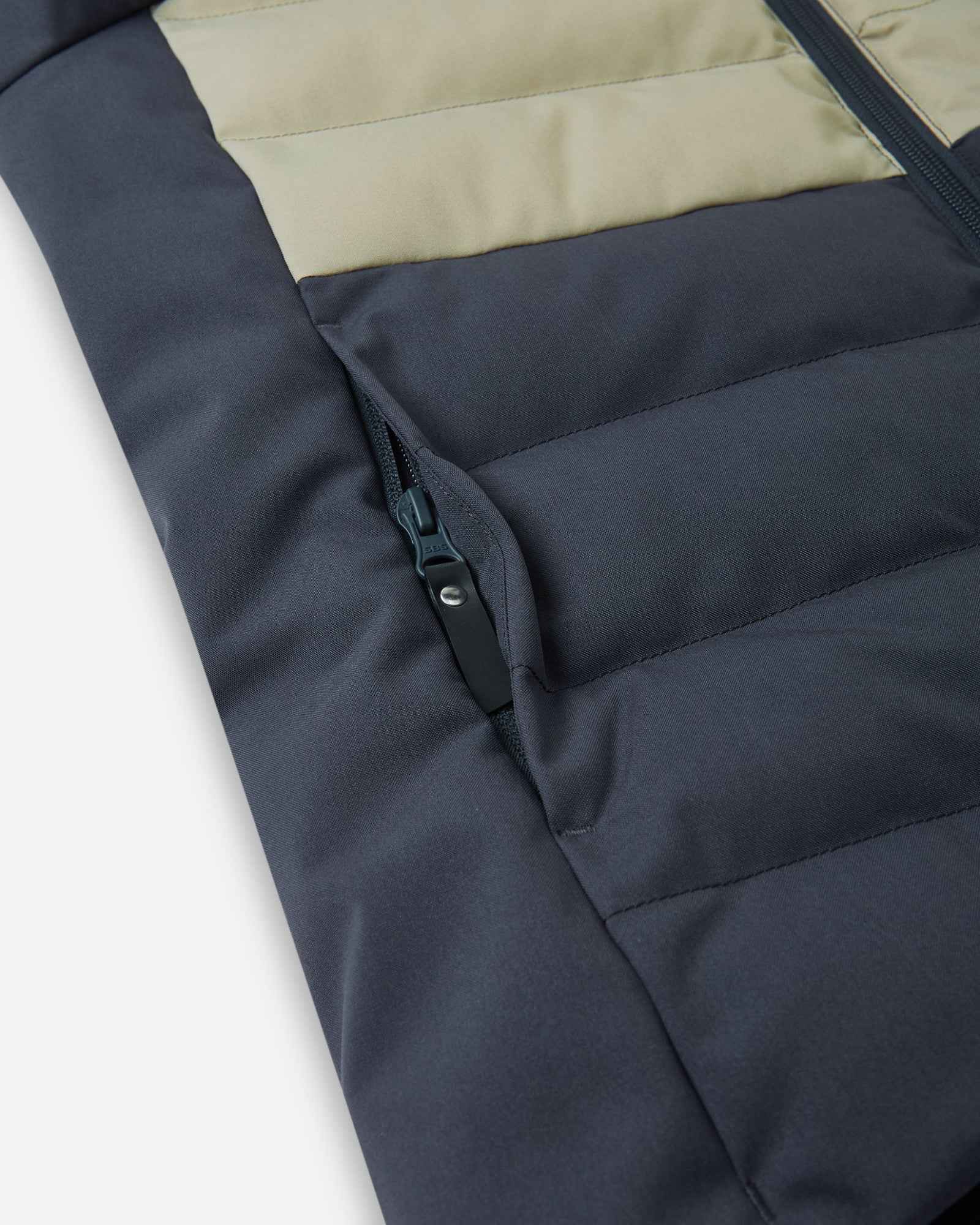 Close-up detail of the secure, hidden front zippered pocket on the quilted body of the Reima Kuosku kids ski jacket in Soft black.