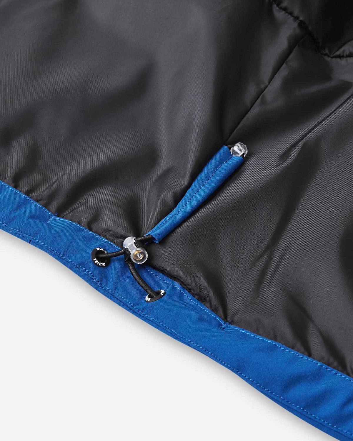 Close-up detail of the interior bottom hem on the Reima Kuosku kids ski jacket in twilight blue, showing the adjustable elastic drawstring cord and locking toggle used to customize the fit and seal in warmth.