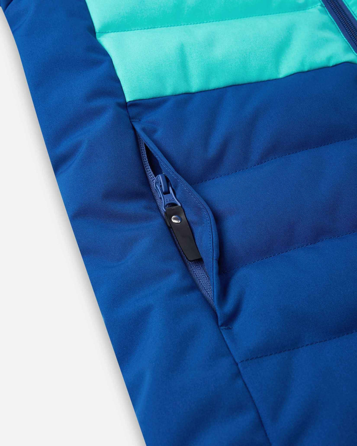 Close-up detail of the secure, hidden front zippered pocket on the quilted twilight blue body of the Reima Kuosku kids ski jacket.