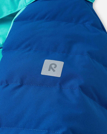 Close-up of the sleeve on the Reima Kuosku kids ski jacket in twilight blue, displaying the reflective Reima 'R' logo patch designed for high visibility during low-light winter activities.