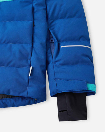 Close-up of the left sleeve on the Reima Kuosku kids ski jacket in twilight blue, showing the zippered ski pass pocket, a horizontal reflective safety strip, adjustable velcro cuff, and inner lycra sleeve.