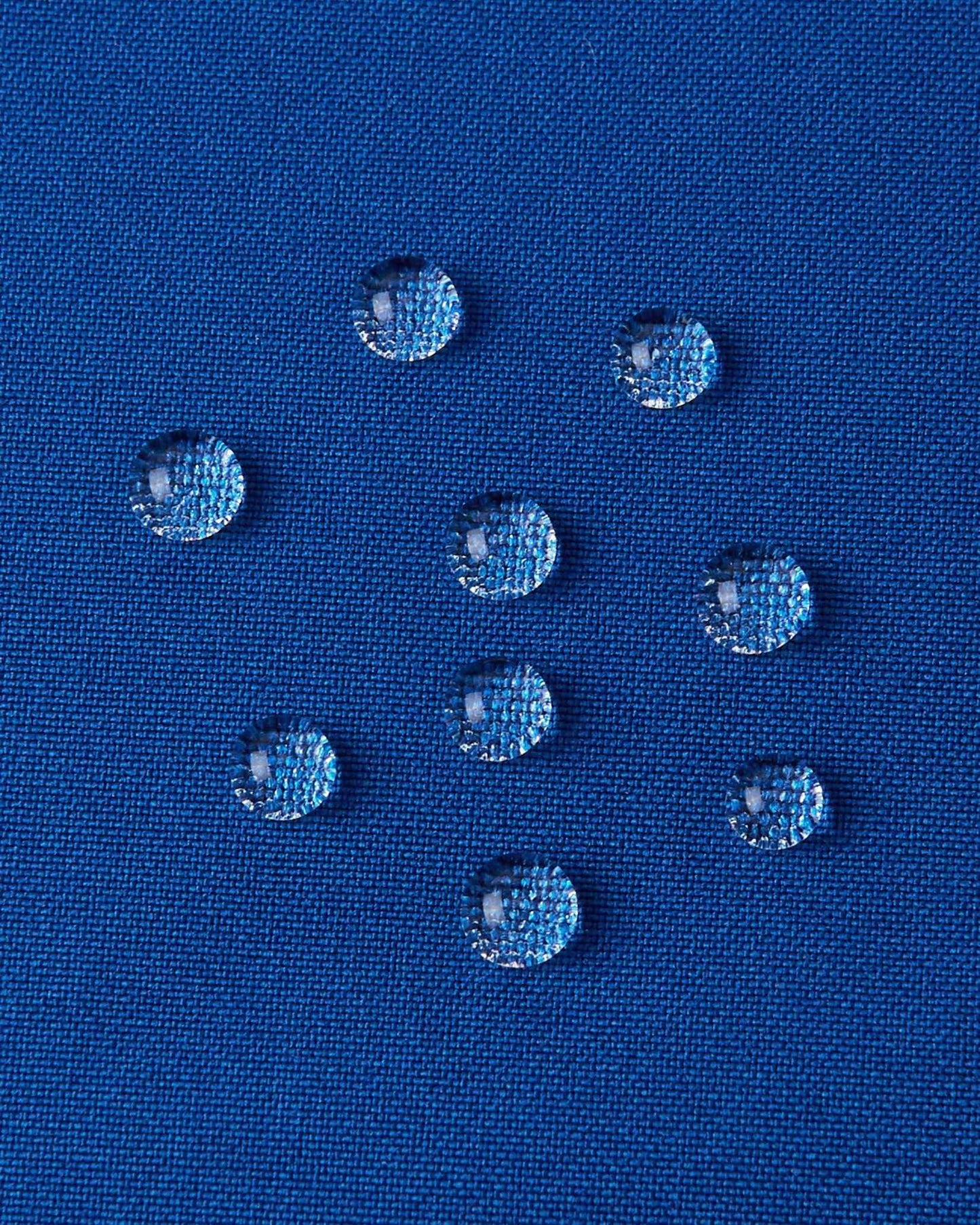 A detailed close-up texture shot of water droplets beading up cleanly on the twilight blue water-repellent fabric of a Reima Kuosku kids ski jacket, demonstrating its durable waterproof performance.
