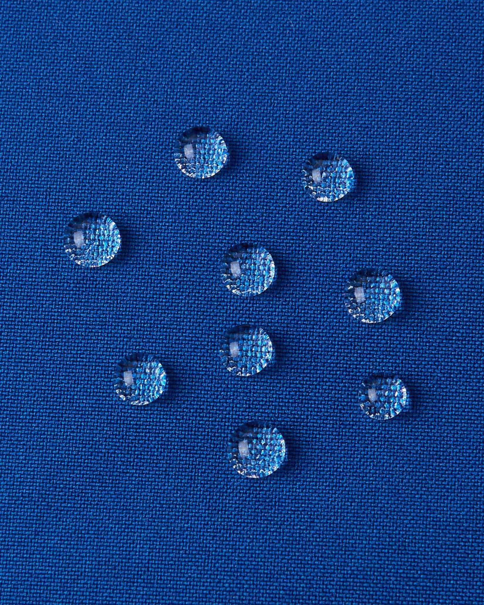 A detailed close-up texture shot of water droplets beading up cleanly on the twilight blue water-repellent fabric of a Reima Kuosku kids ski jacket, demonstrating its durable waterproof performance.