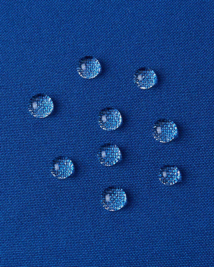 A detailed close-up texture shot of water droplets beading up cleanly on the twilight blue water-repellent fabric of a Reima Kuosku kids ski jacket, demonstrating its durable waterproof performance.