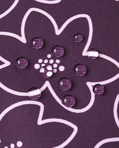 Macro photography of water droplets perfectly beading on the deep purple floral fabric of the Reima Kurikka snowsuit, illustrating the advanced dirt-repellent and waterproof textile technology.