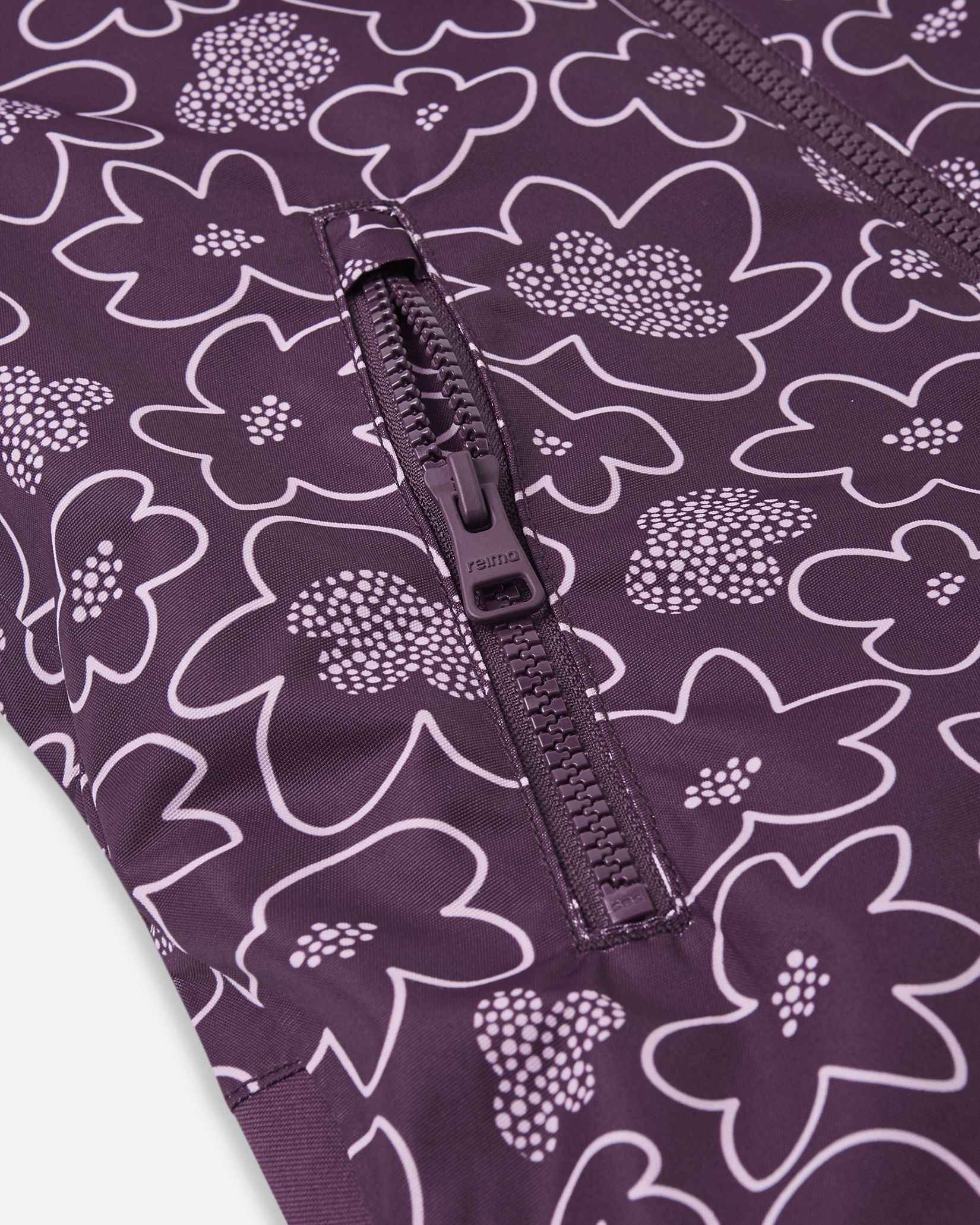 Close-up of the securely zippered chest pocket embedded within the deep purple and white floral pattern of the Reima Kurikka kids' winter overall.