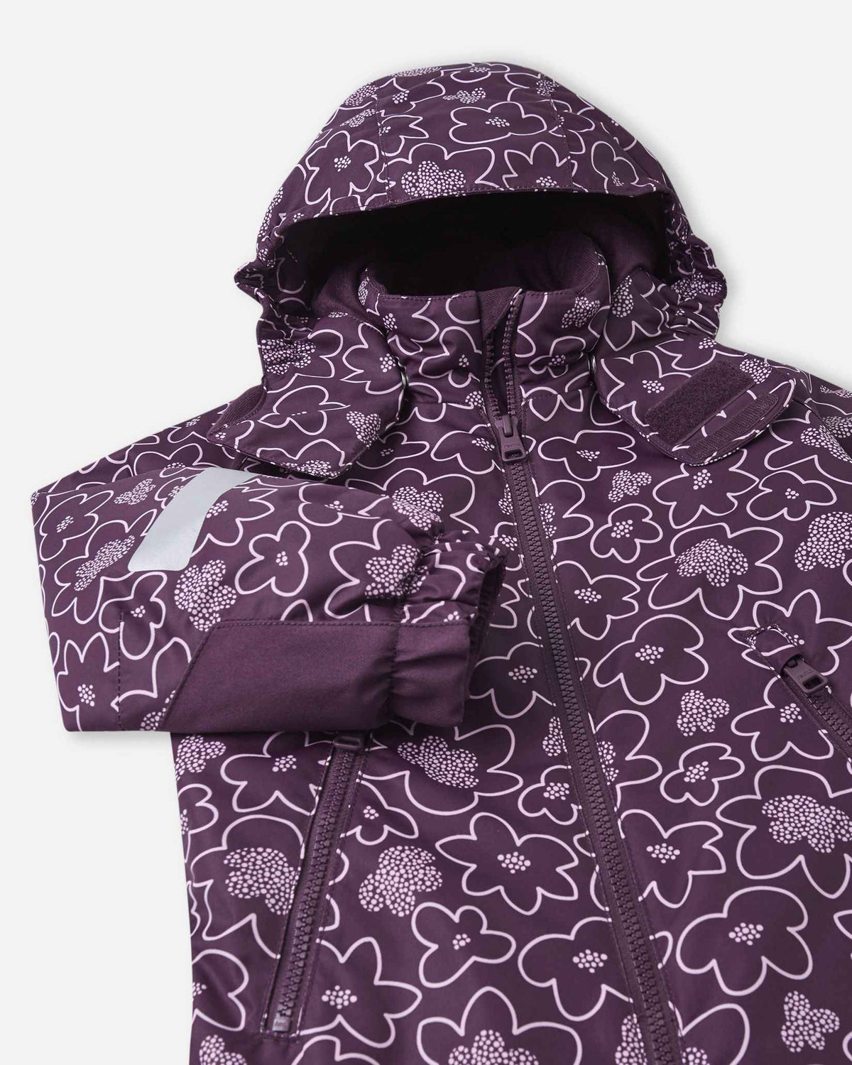 Close-up on the chest and hood of the deep purple Reima Kurikka winter suit, emphasizing the smooth center zipper, protective storm flap, and the charming white flower outline pattern.