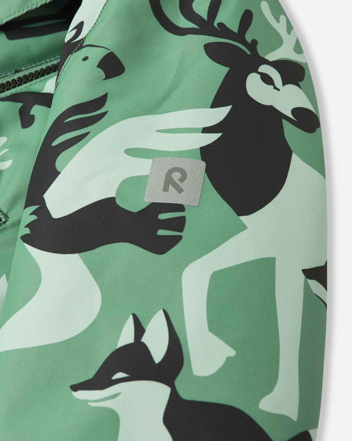 Close-up of the reflective Reima logo patch on the sleeve of the Kurikka green clay snowsuit, designed for high visibility in winter conditions.