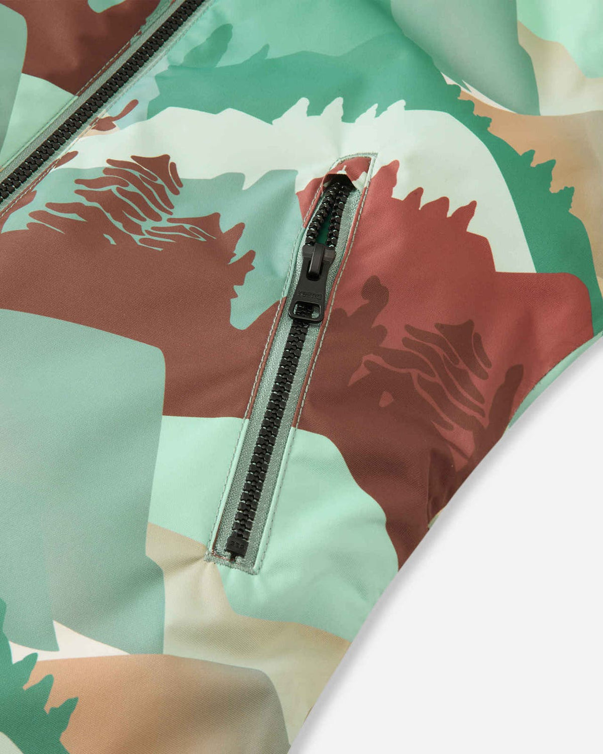 Close-up of the front zippered pocket on the Reima Kurikka kids' snowsuit, showing the durable black zipper hardware against the stone green mountain pattern fabric.