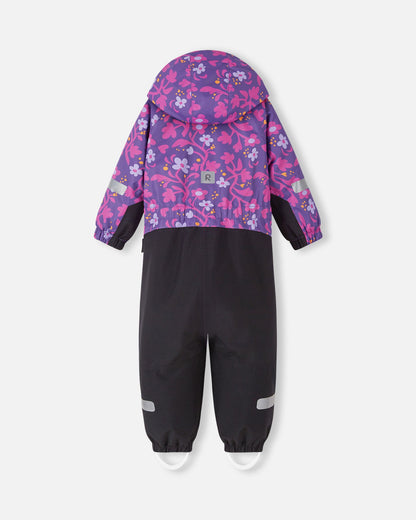 Back view of the Reima Kurikka kids' winter snowsuit in a plum purple floral print, showing the attached hood, a cinched elastic waist for a better fit, and reflective safety patches on the sleeves and legs.