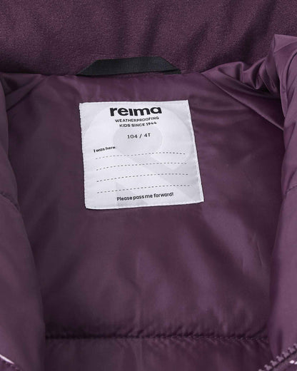Interior view of the Reima Kurikka snowsuit showcasing the size 104 or 4T label, Reima weatherproofing certification, and a dedicated blank name tag for easy identification at daycare or ski school.