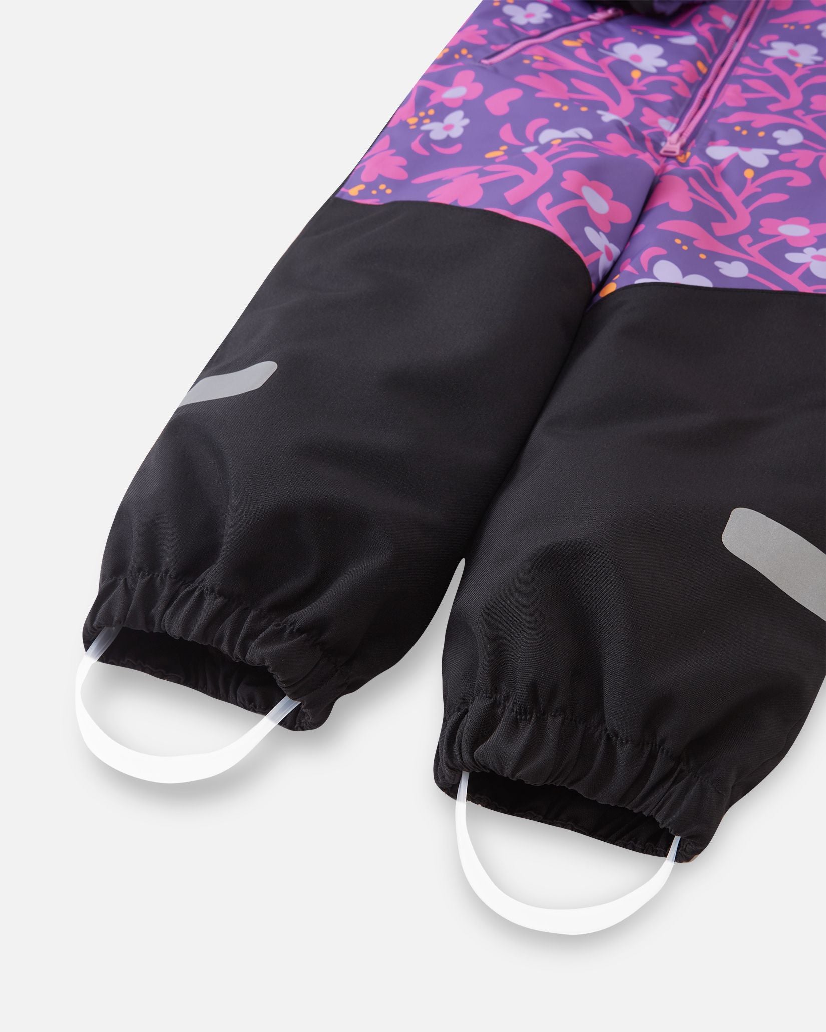 Close-up of the black reinforced leg hems on the Reima Kurikka snowsuit, showcasing the elastic ankle cuffs, reflective safety strips, and durable white silicone foot loops designed to stretch over boots and keep snow out.