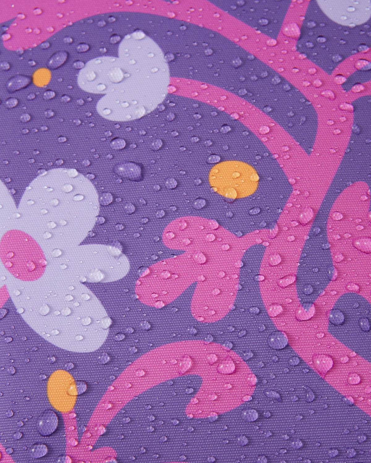 Macro close-up of water droplets beading and rolling off the plum purple floral Reimatec fabric of the Kurikka snowsuit, demonstrating its advanced waterproof and weather-resistant technology.