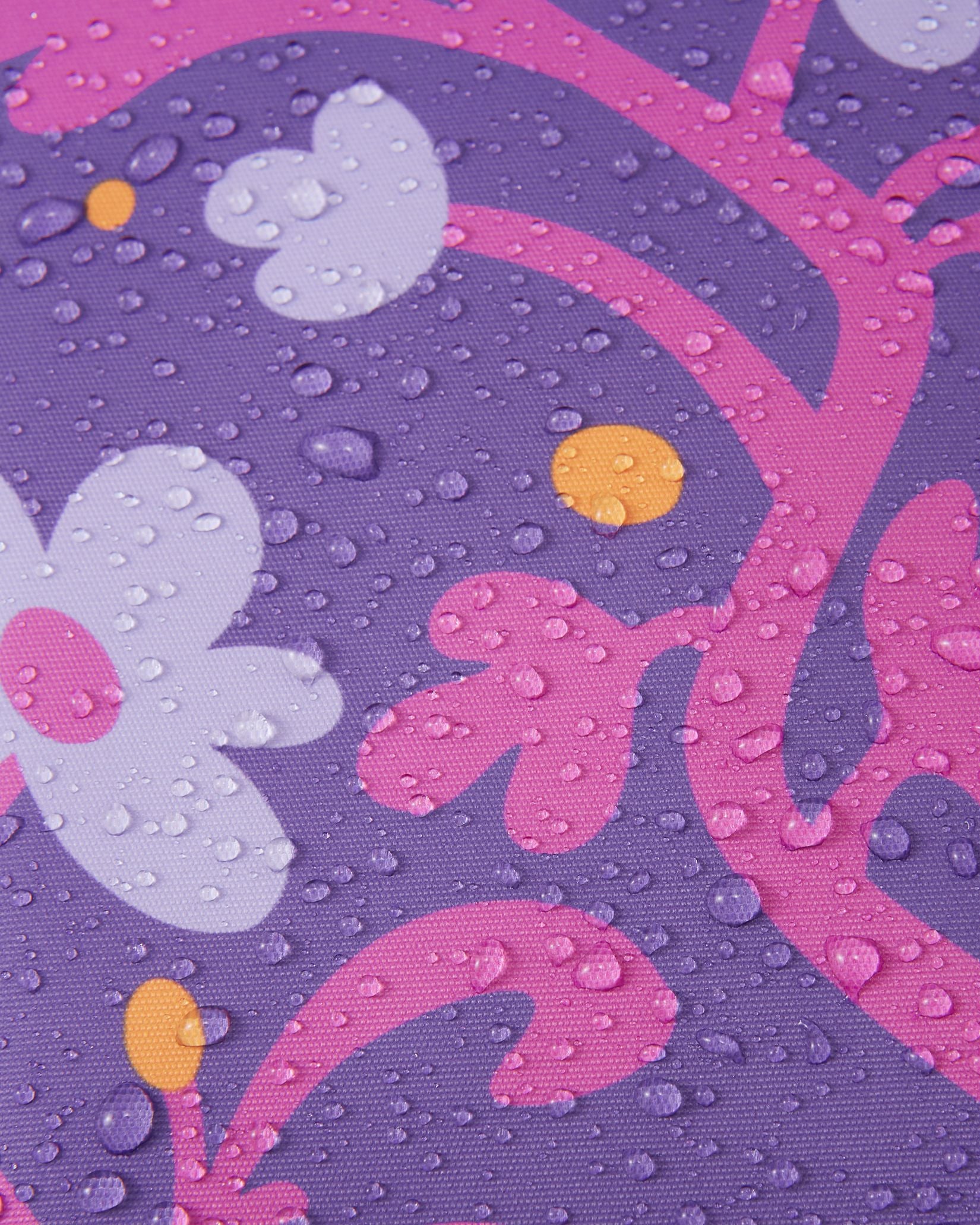 Macro close-up of water droplets beading and rolling off the plum purple floral Reimatec fabric of the Kurikka snowsuit, demonstrating its advanced waterproof and weather-resistant technology.