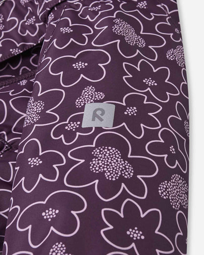 Detailed shot of the sleeve on the floral deep purple Reima Kurikka children's overall, focusing on the high-visibility reflective Reima badge integrated into the fabric to enhance child safety during dark winter afternoons.