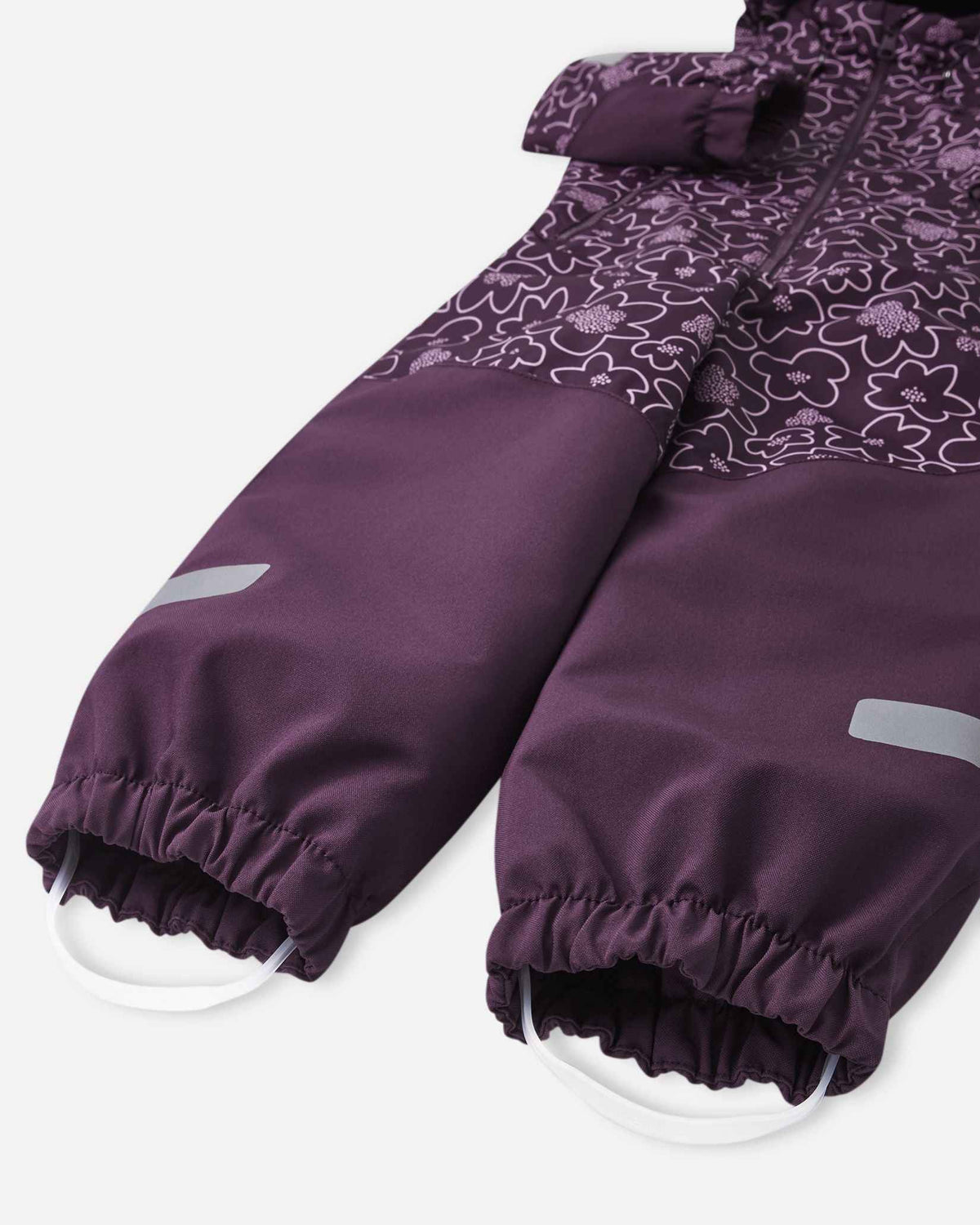 Detail view of the solid deep purple lower legs on the Reima Kurikka snowsuit, displaying the gathered elastic cuffs, secure white silicone foot loops, and safety reflective patches.