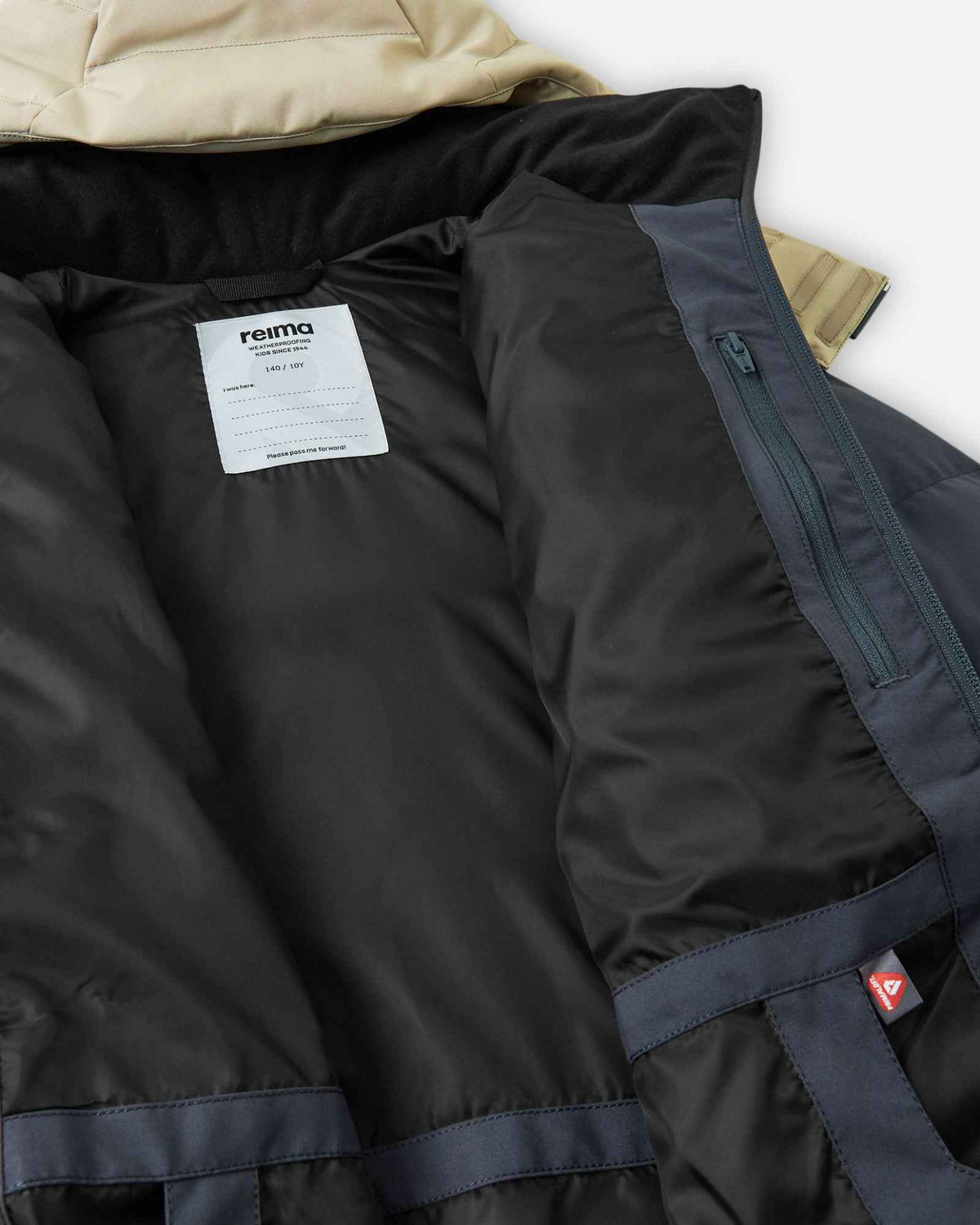 Interior view of the Reima Kusoku kids ski jacket in Soft black, highlighting the smooth black inner lining, a white Reima brand name tag for personalization, a secure zippered inner chest pocket, and a soft fleece-lined collar designed for added comfort and winter warmth.