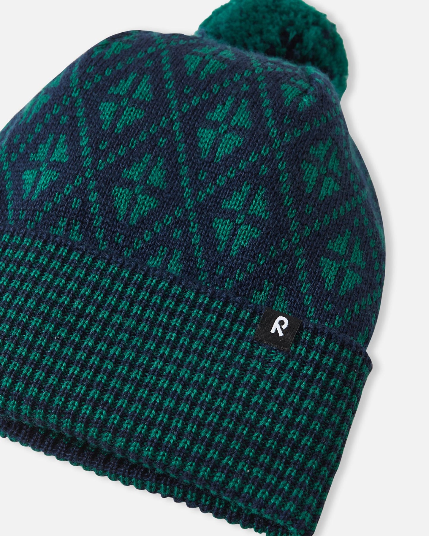 Angled side view of the navy blue Reima Kuurassa kids' merino wool beanie hat, highlighting the small black Reima logo tag on the ribbed brim and the textured knit pattern.