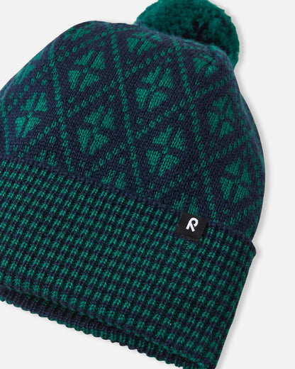Angled side view of the navy blue Reima Kuurassa kids' merino wool beanie hat, highlighting the small black Reima logo tag on the ribbed brim and the textured knit pattern.