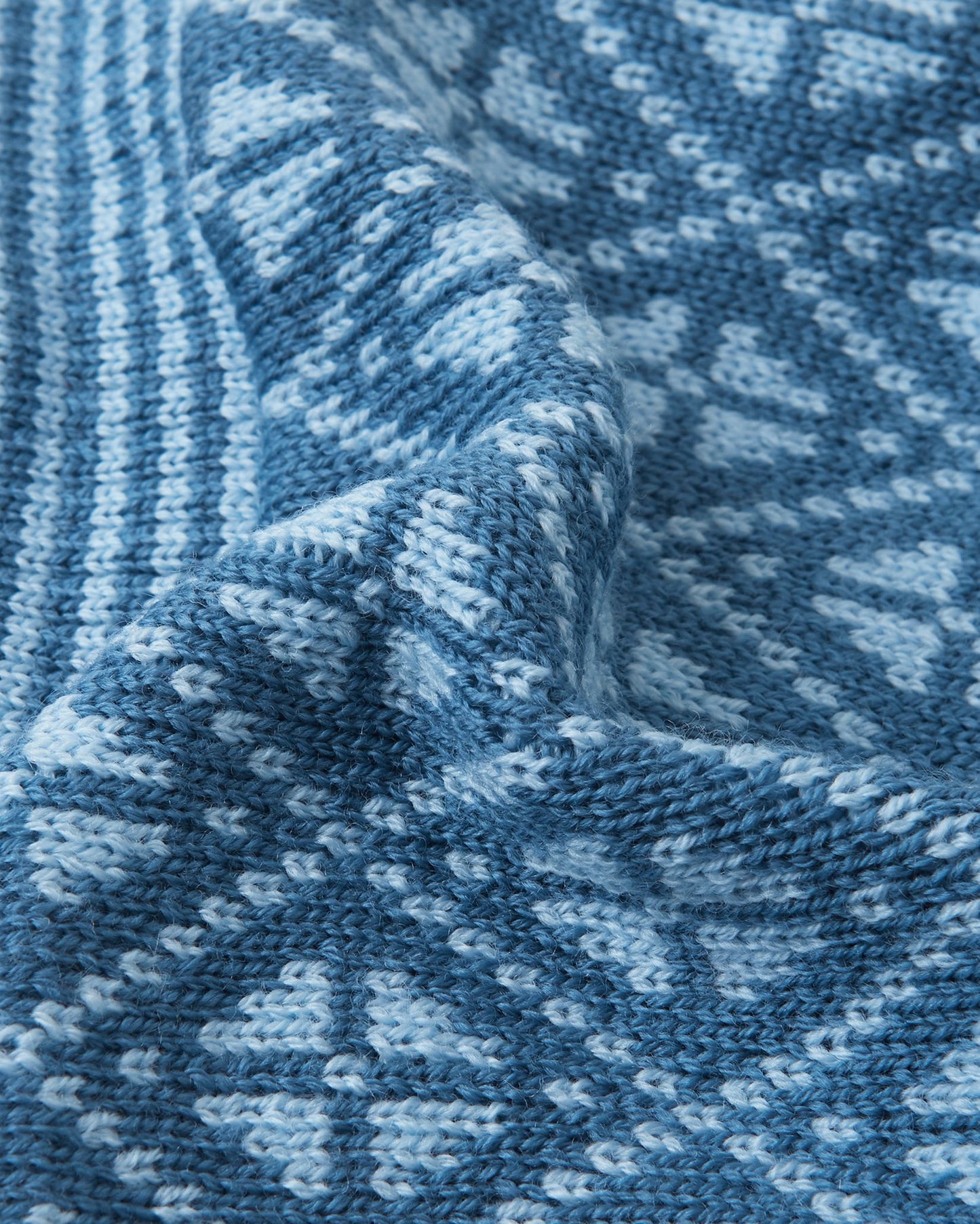 Macro close-up of the premium knitted merino wool texture on the ocean blue Reima Kuurassa kids' beanie, demonstrating the intricate Nordic pattern and the soft, temperature-regulating winter yarn.