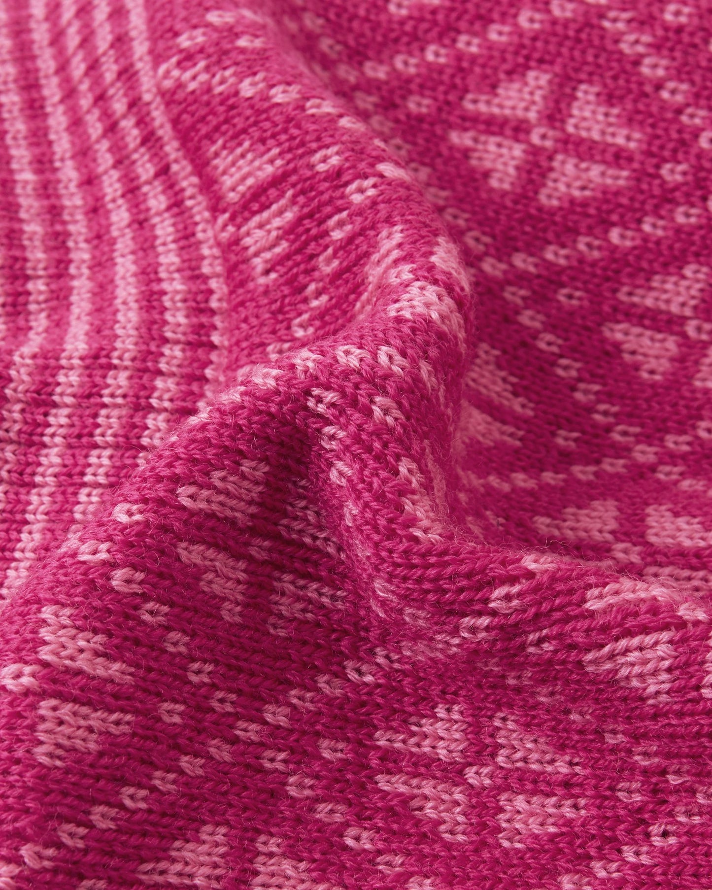Macro close-up of the premium knitted merino wool texture on the rosy berry Reima Kuurassa kids' beanie, demonstrating the intricate Nordic pattern and the soft, temperature-regulating winter yarn.