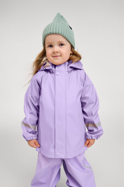 Lifestyle portrait of a young child happily wearing the Reima Lampi raincoat in blooming lilac, paired with matching rain pants and a mint green knit beanie, highlighting the jacket's comfortable, flexible fit designed for active outdoor play.