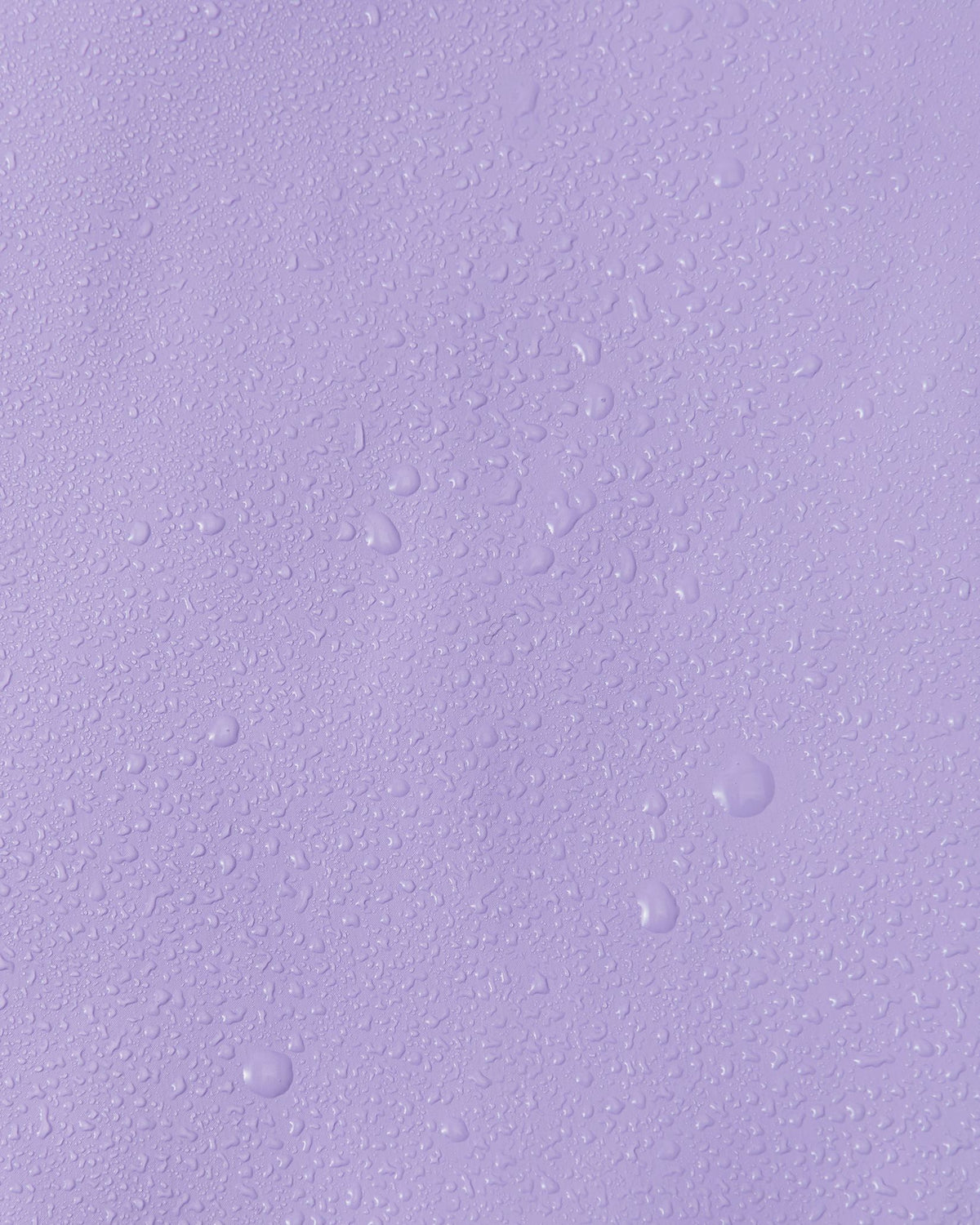 Close-up macro shot showing water droplets tightly beading on the smooth, waterproof polyurethane surface of the Reima Lampi blooming lilac raincoat, demonstrating its superior ability to repel water and keep children completely dry during heavy rain.