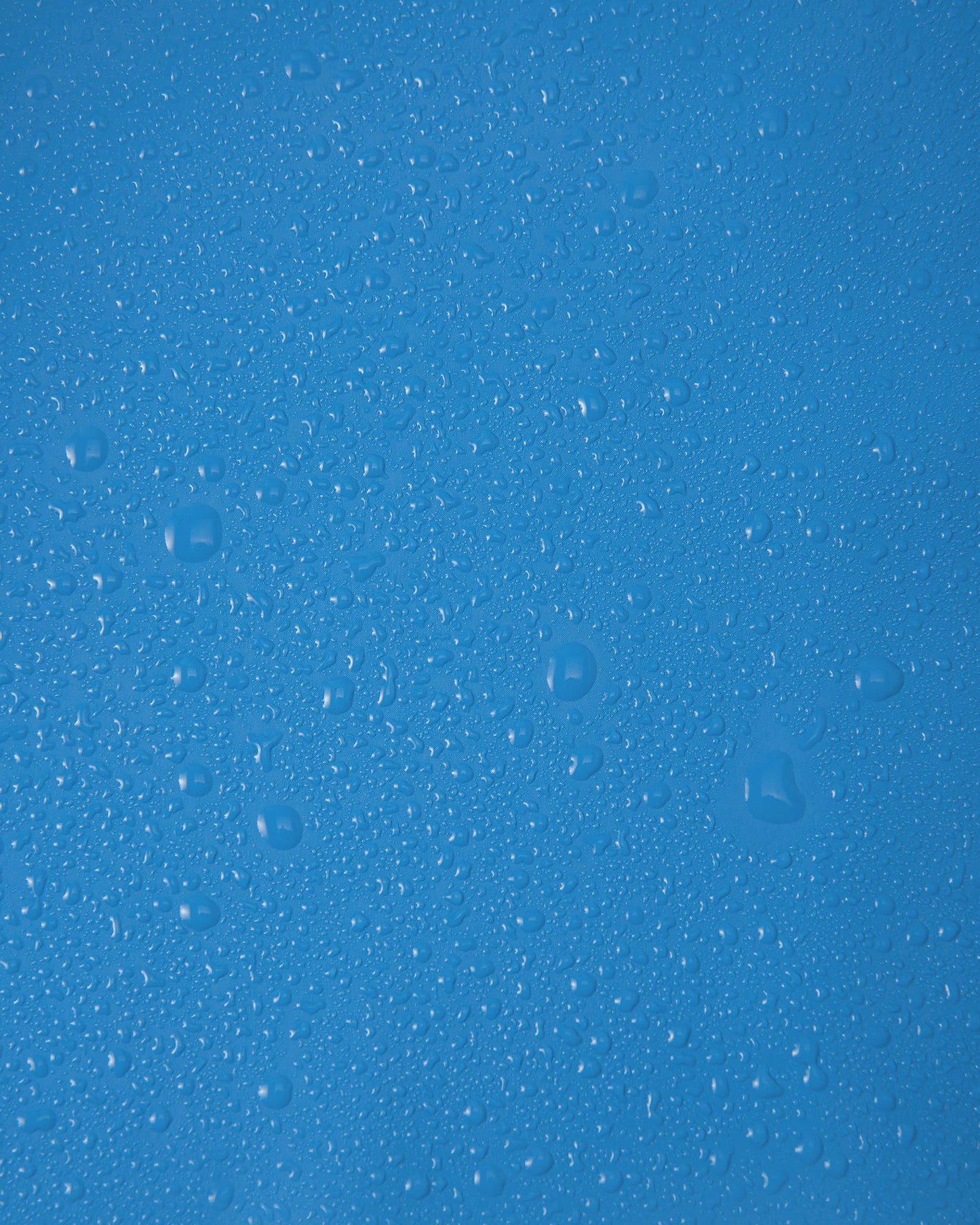 Close-up macro shot of water droplets tightly beading on the smooth, cool blue polyurethane surface of the Reima Lampi raincoat, showcasing the material's highly effective waterproof finish that reliably keeps children dry during heavy downpours.