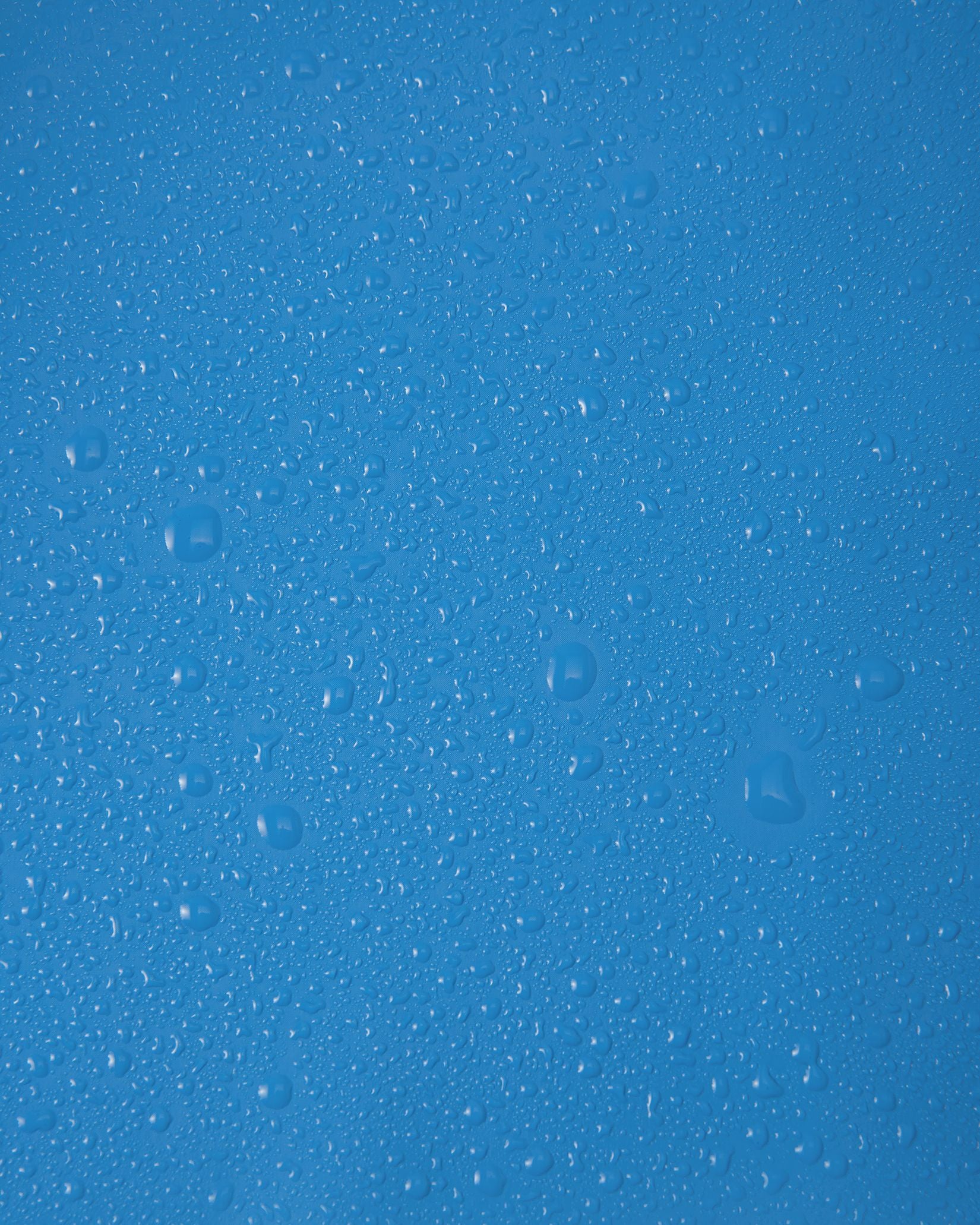 Close-up macro shot of water droplets tightly beading on the smooth, cool blue polyurethane surface of the Reima Lampi raincoat, showcasing the material's highly effective waterproof finish that reliably keeps children dry during heavy downpours.