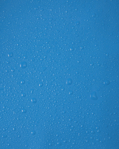 Close-up macro shot of water droplets tightly beading on the smooth, cool blue polyurethane surface of the Reima Lampi raincoat, showcasing the material's highly effective waterproof finish that reliably keeps children dry during heavy downpours.