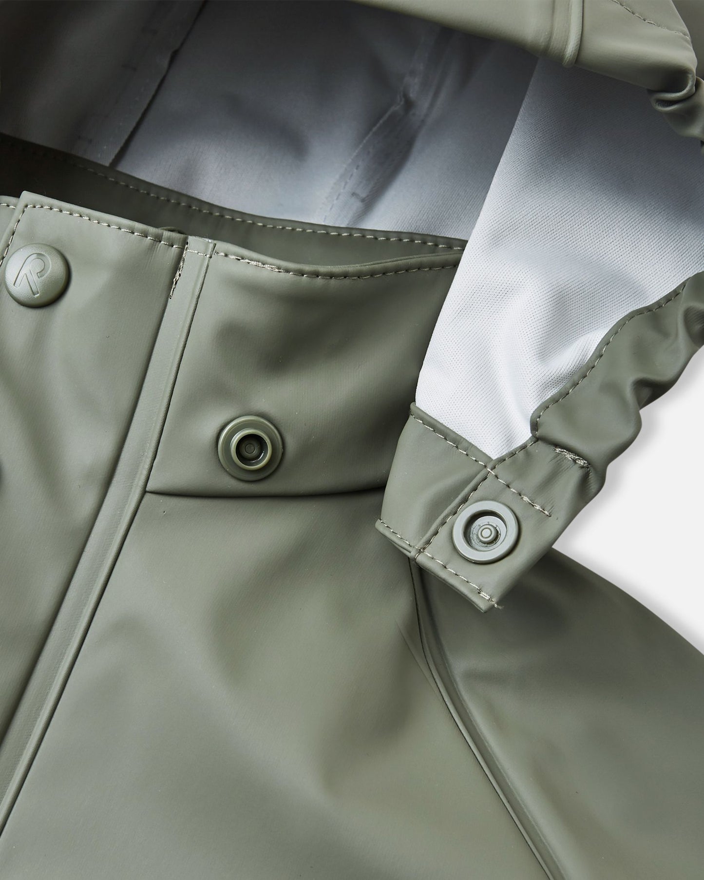 Detailed macro shot of the Reima Lampi raincoat collar in greyish-green, focusing on the child-safe snap button attachments that ensure the hood easily and safely detaches if it accidentally gets caught on playground equipment or tree branches.