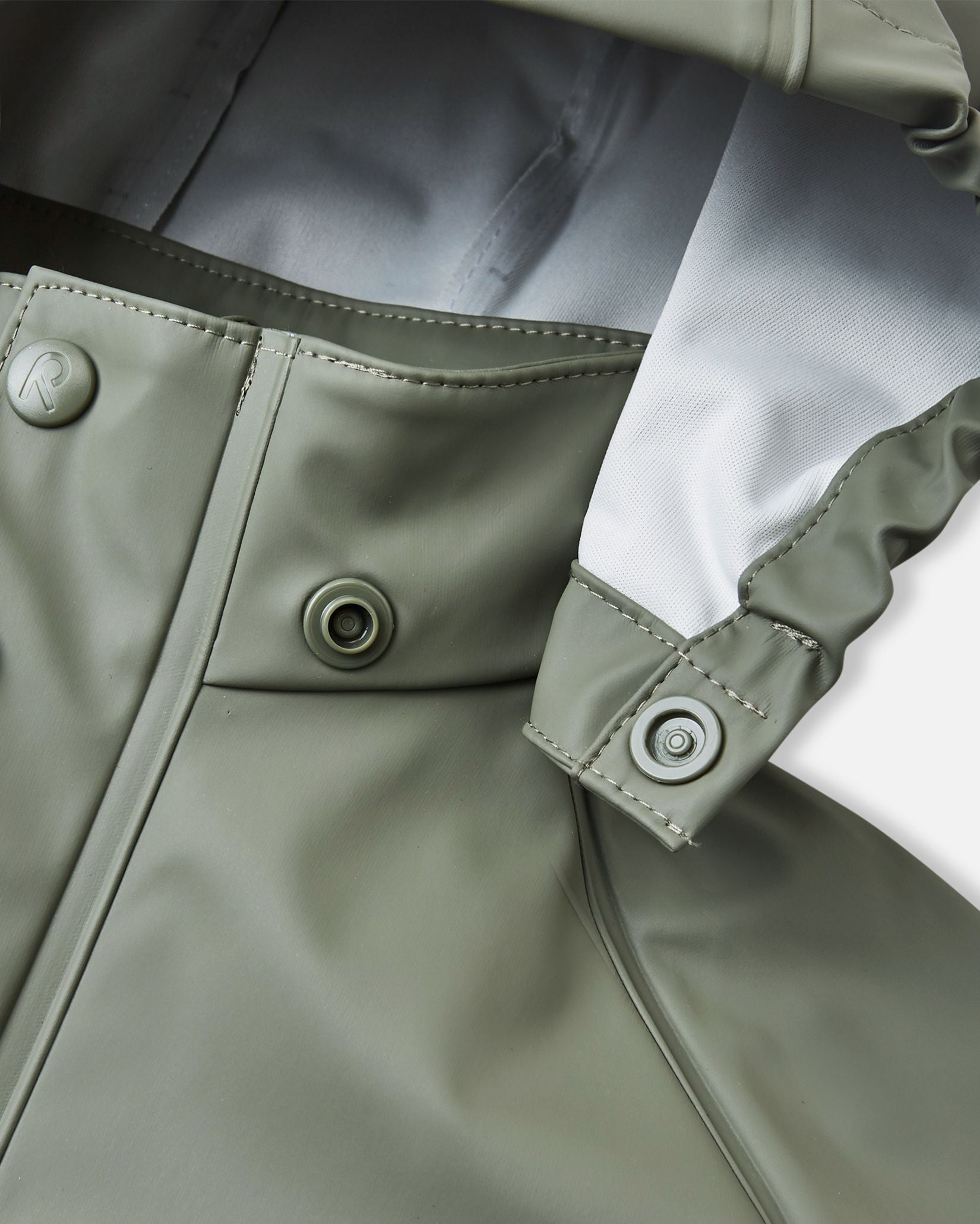 Detailed macro shot of the Reima Lampi raincoat collar in greyish-green, focusing on the child-safe snap button attachments that ensure the hood easily and safely detaches if it accidentally gets caught on playground equipment or tree branches.
