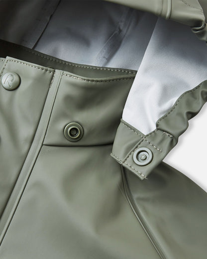 Detailed macro shot of the Reima Lampi raincoat collar in greyish-green, focusing on the child-safe snap button attachments that ensure the hood easily and safely detaches if it accidentally gets caught on playground equipment or tree branches.