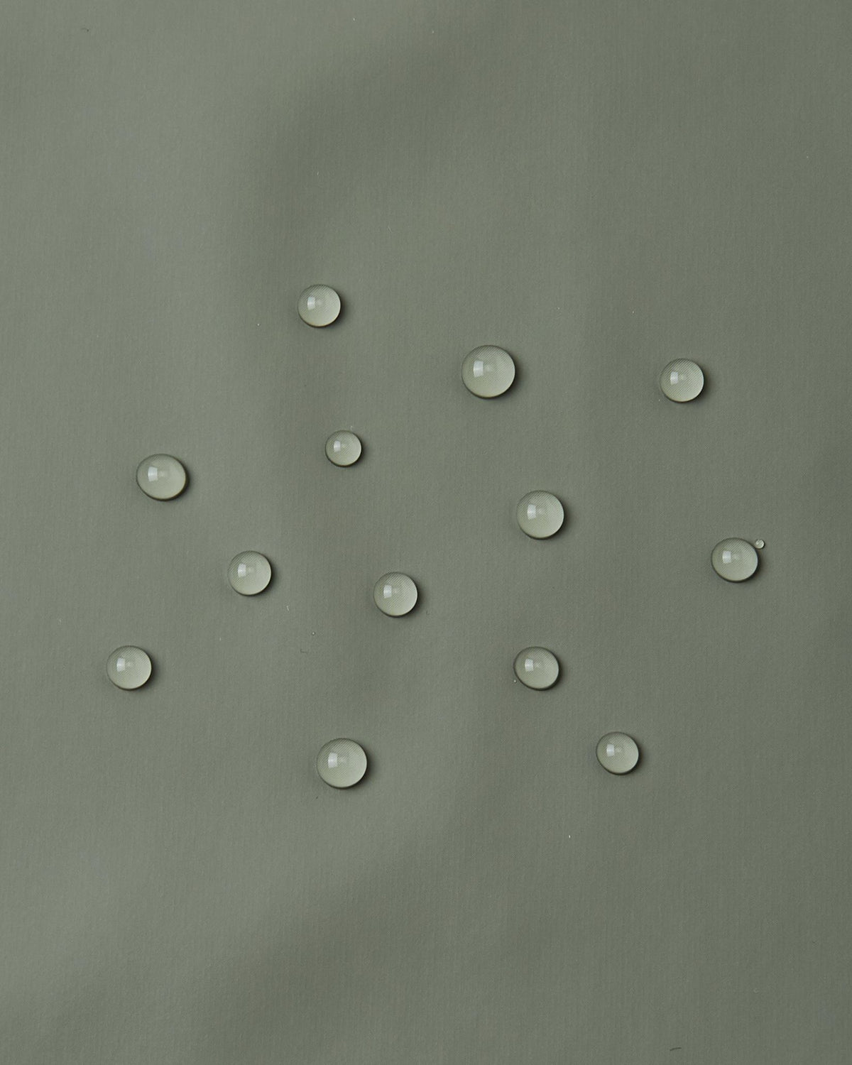 Close-up demonstration of water droplets tightly beading and rolling off the smooth waterproof polyurethane surface of the Reima Lampi greyish-green raincoat, proving its effectiveness at keeping kids completely dry during heavy downpours.