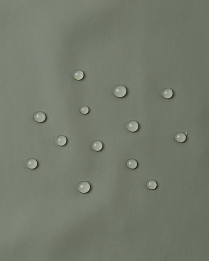 Close-up demonstration of water droplets tightly beading and rolling off the smooth waterproof polyurethane surface of the Reima Lampi greyish-green raincoat, proving its effectiveness at keeping kids completely dry during heavy downpours.