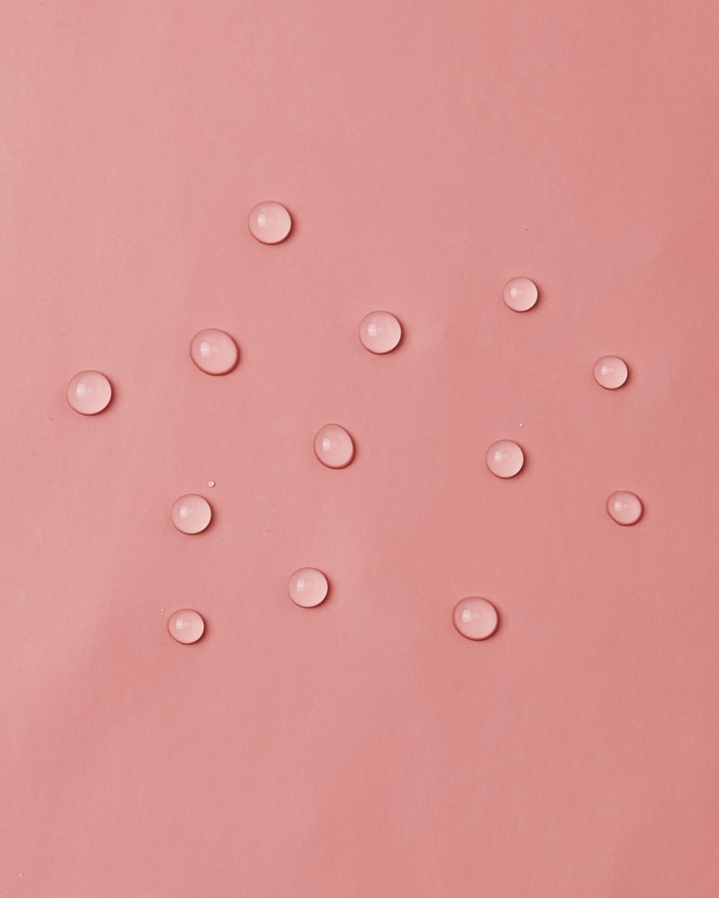 Macro close-up demonstrating water droplets perfectly beading and sitting lightly on top of the smooth waterproof polyurethane surface of the Reima Lampi rose blush raincoat, highlighting the material's excellent rain-repellent capabilities.