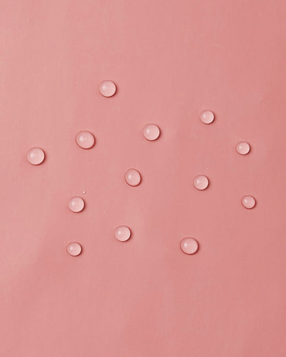 Macro close-up demonstrating water droplets perfectly beading and sitting lightly on top of the smooth waterproof polyurethane surface of the Reima Lampi rose blush raincoat, highlighting the material's excellent rain-repellent capabilities.