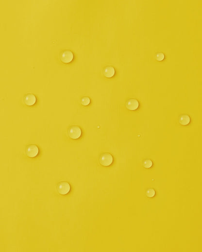 Macro close-up of water droplets perfectly beading on the smooth, bright yellow waterproof polyurethane surface of the Reima Lampi raincoat, demonstrating its excellent ability to repel rain and keep kids completely dry.