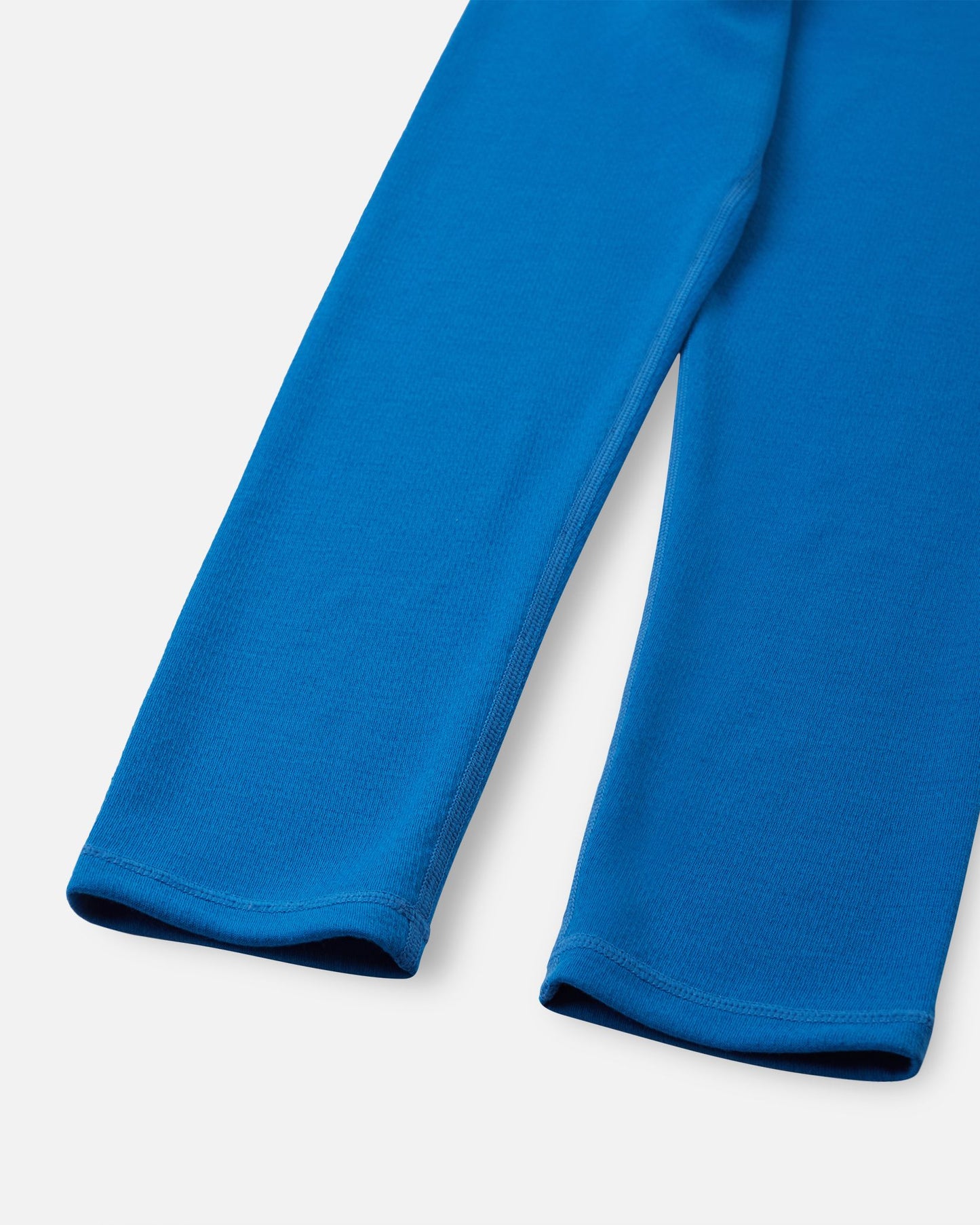 Close-up of the ankle cuffs and flatlock seams on the bright blue Reima Lani kids' thermal base layer pants, built to prevent chafing during active play.