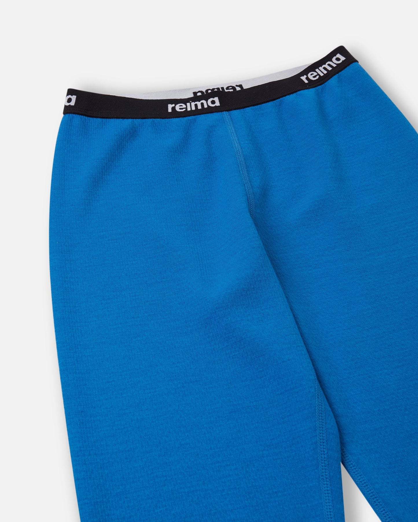 Detailed close-up of the soft elastic waistband featuring the Reima logo on the bright blue Lani kids' thermal base layer pants.