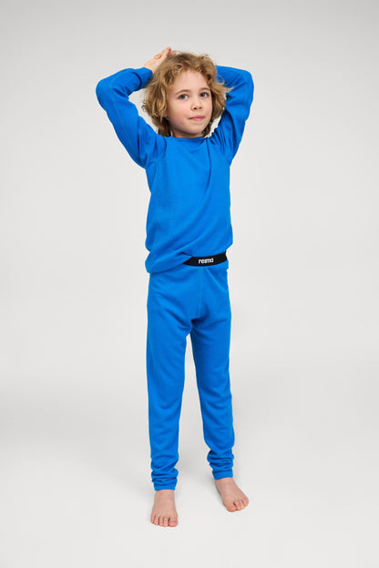 Lifestyle portrait of a young child modeling the bright blue Reima Lani kids' Thermolite base layer set, demonstrating its comfortable fit and flexibility for winter sports and daily wear.