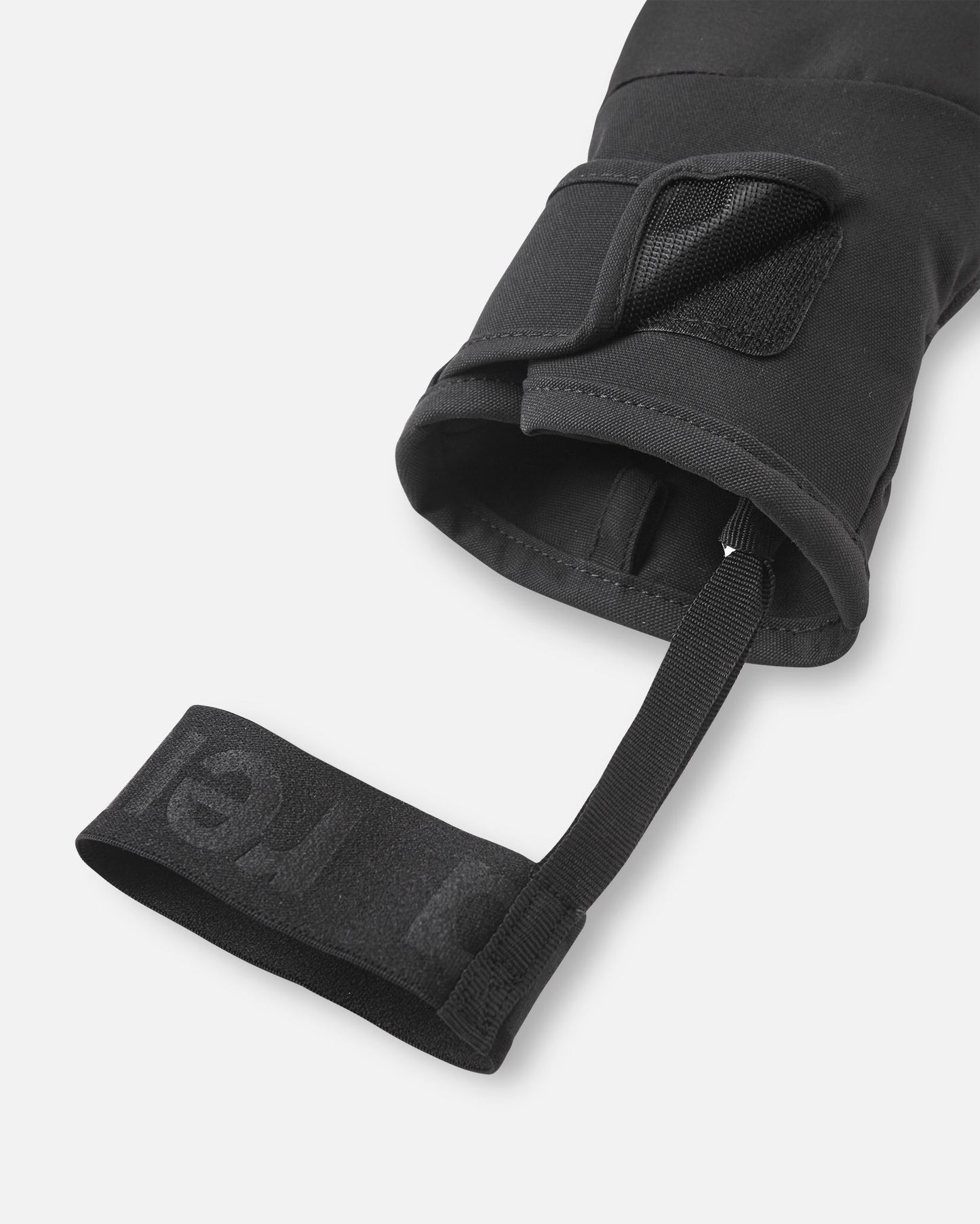 Close-up detail of the cuff on the black Reima Lapases kids' ski mittens, emphasizing the adjustable hook-and-loop closure strap and the black elastic safety wrist leash designed to prevent dropped mittens on the chairlift.