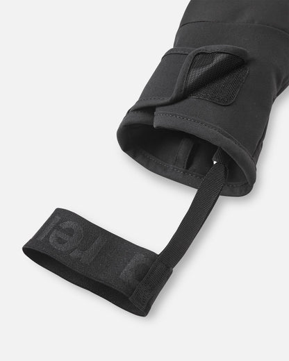 Close-up detail of the cuff on the black Reima Lapases kids' ski mittens, emphasizing the adjustable hook-and-loop closure strap and the black elastic safety wrist leash designed to prevent dropped mittens on the chairlift.