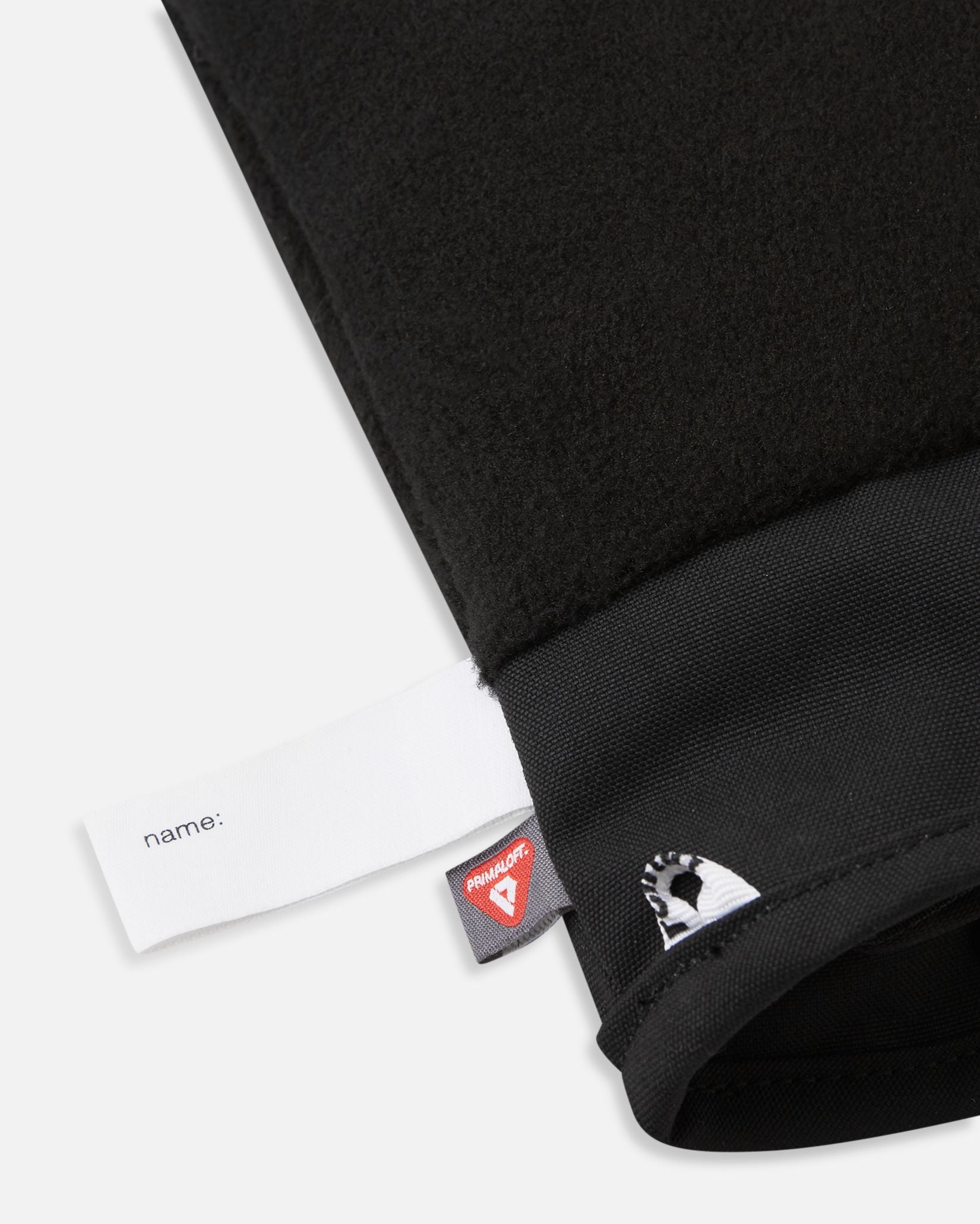 Detail of the inner cuff of the blooming lilac Reima Lapases kids' ski mittens, revealing the soft black thermal fleece lining, a blank customizable name tag, and the 100% recycled PrimaLoft insulation label for premium winter warmth.