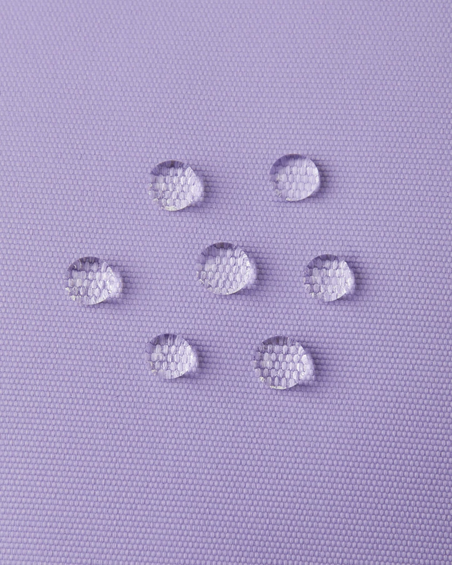 Macro close-up of water droplets actively beading and rolling off the blooming lilac outer shell of the Reima Lapases kids' ski mittens, demonstrating the high-performance waterproof Hipora membrane and dirt-repellent finish.