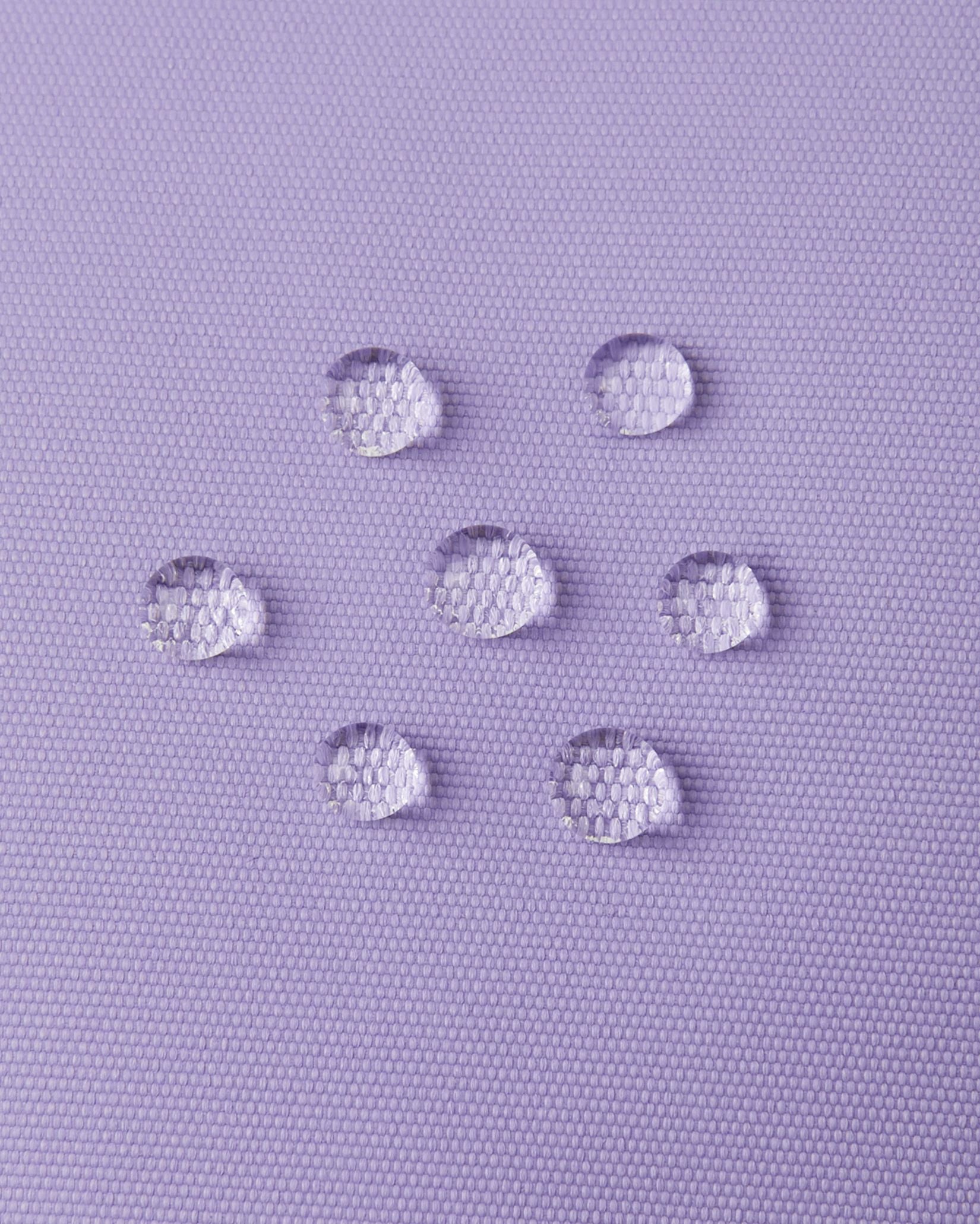 Macro close-up of water droplets actively beading and rolling off the blooming lilac outer shell of the Reima Lapases kids' ski mittens, demonstrating the high-performance waterproof Hipora membrane and dirt-repellent finish.