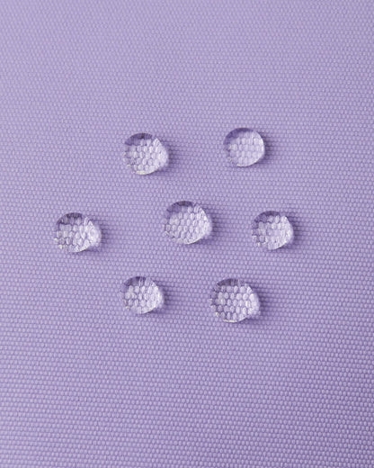 Macro close-up of water droplets actively beading and rolling off the blooming lilac outer shell of the Reima Lapases kids' ski mittens, demonstrating the high-performance waterproof Hipora membrane and dirt-repellent finish.