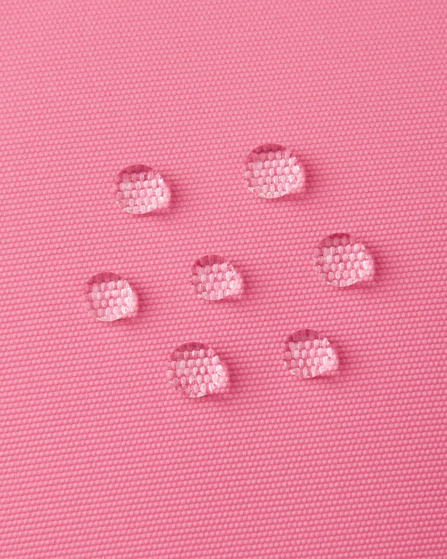 Macro close-up of water droplets actively beading and rolling off the soft coral outer shell of the Reima Lapases kids' ski mittens, demonstrating the high-performance waterproof Hipora insert and breathable technical fabric.
