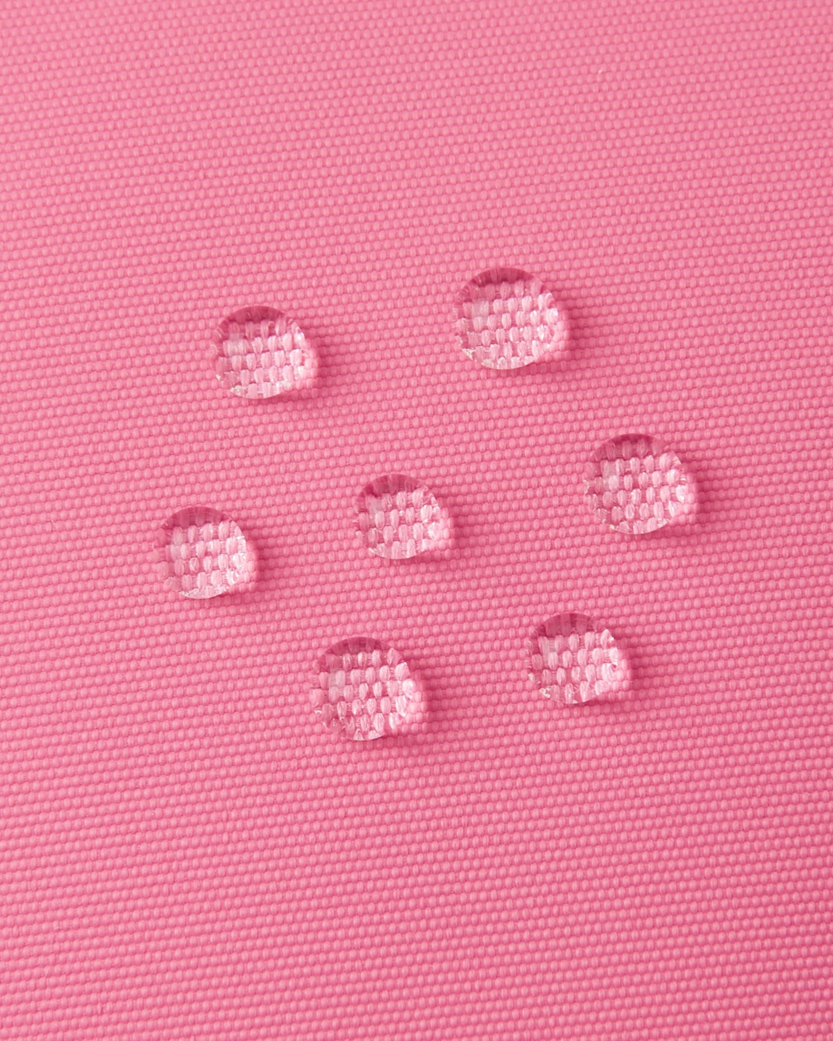 Macro close-up of water droplets actively beading and rolling off the soft coral outer shell of the Reima Lapases kids' ski mittens, demonstrating the high-performance waterproof Hipora insert and breathable technical fabric.