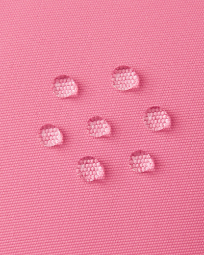 Macro close-up of water droplets actively beading and rolling off the soft coral outer shell of the Reima Lapases kids' ski mittens, demonstrating the high-performance waterproof Hipora insert and breathable technical fabric.